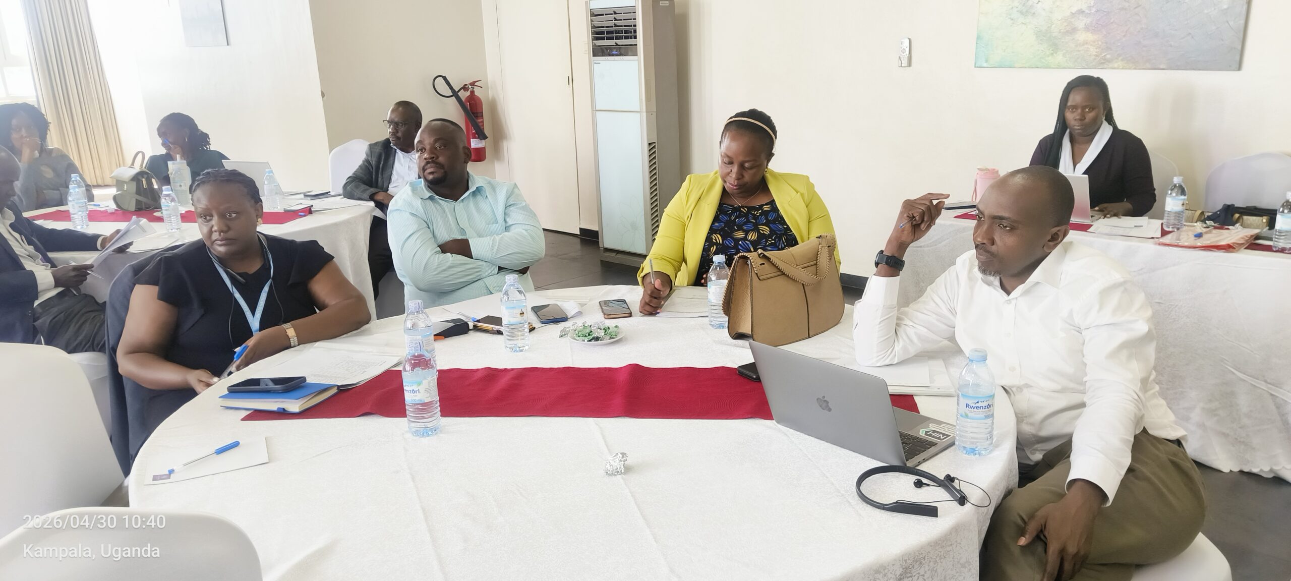 A group of professionals seated around a table in a meeting room, taking notes and using laptops during a workshop in Kampala, Uganda (2026/04/30).
