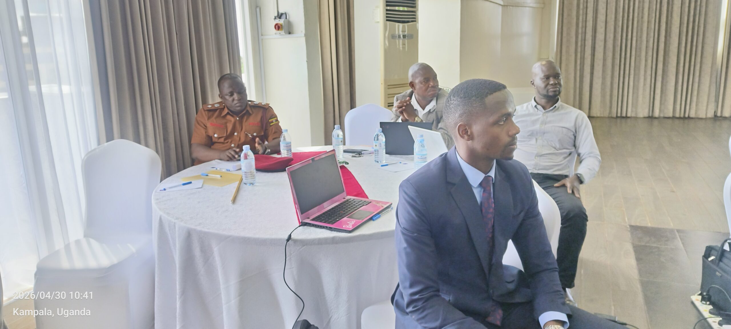 Group of men seated around a round table in a conference room with laptops and water bottles during a meeting in Uganda