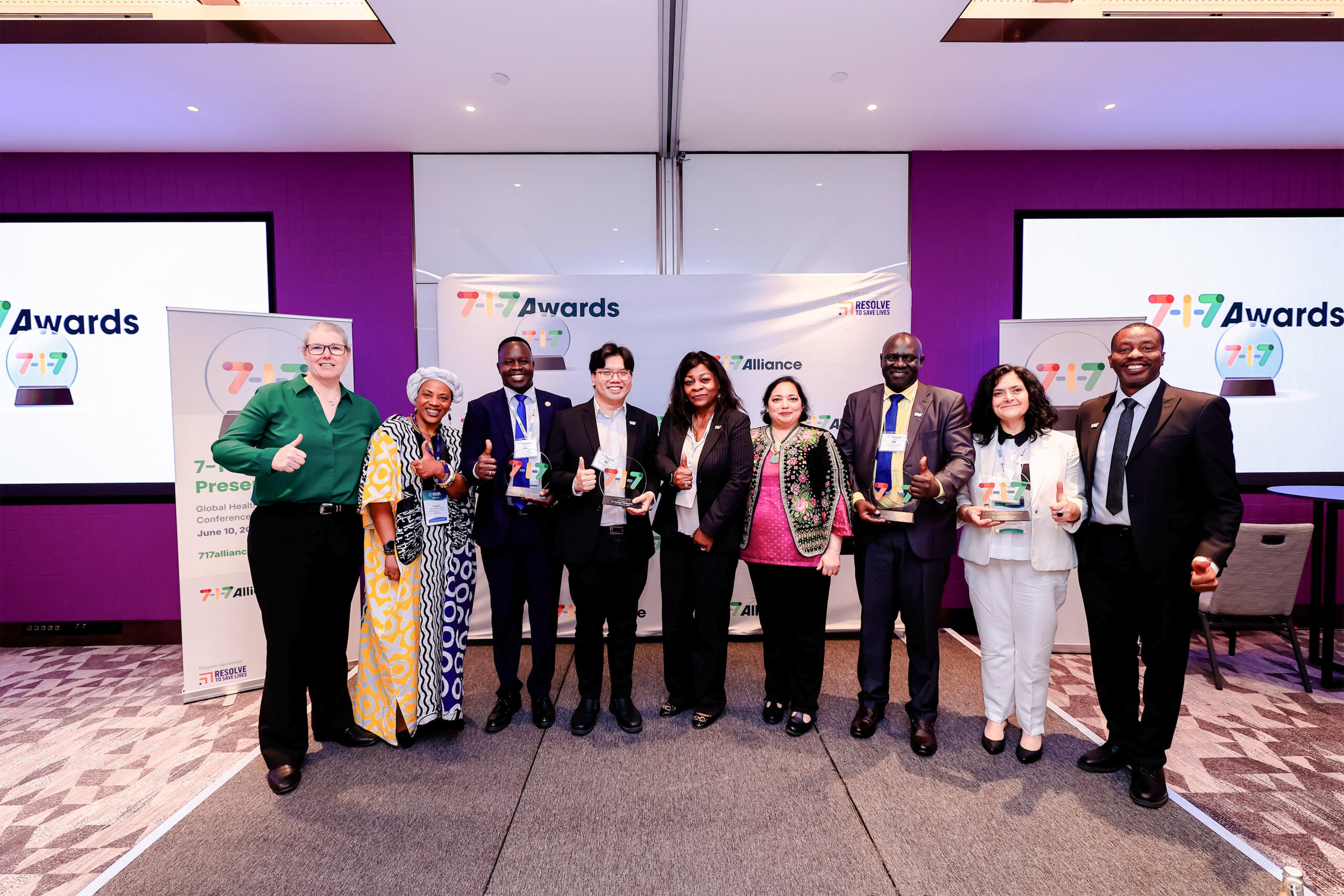 Group of diverse professionals on stage at a 7-7 Awards event, posing with glass trophies in front of a purple backdrop.